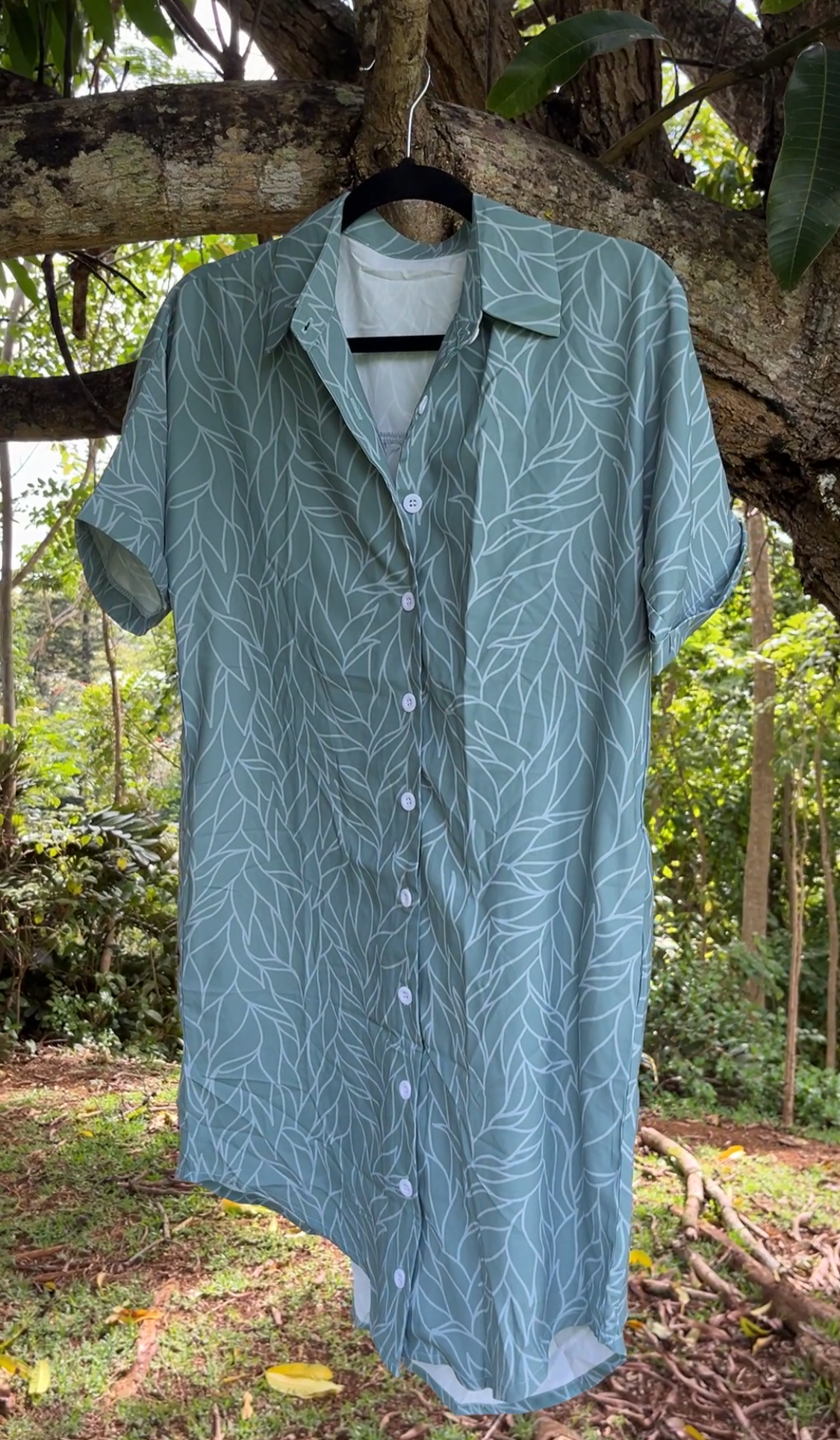 green patterned womens aloha shirt dress hanging on a tree branch with a natural background